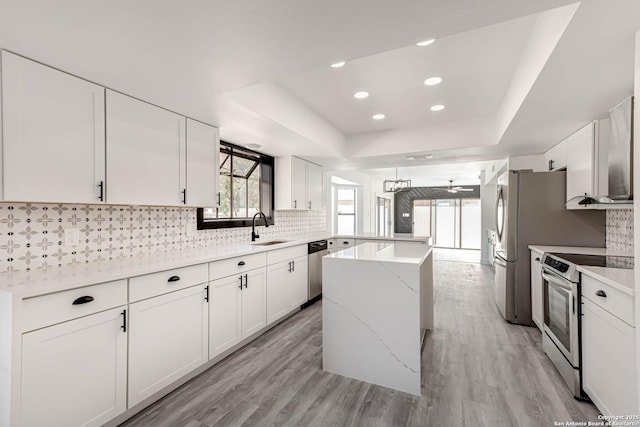 kitchen featuring stainless steel appliances, a peninsula, light wood-style floors, tasteful backsplash, and a raised ceiling