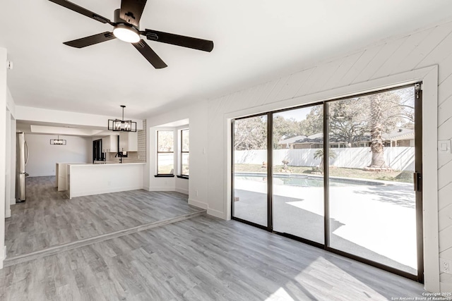 unfurnished living room with light wood-style floors, baseboards, and ceiling fan with notable chandelier