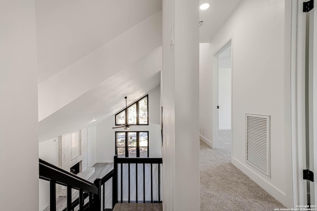 hall featuring baseboards, visible vents, lofted ceiling, carpet flooring, and an upstairs landing