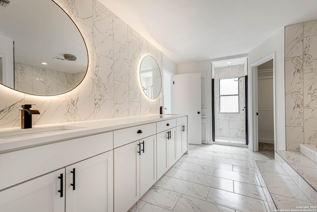 full bathroom featuring marble finish floor, a marble finish shower, double vanity, a sink, and stone wall