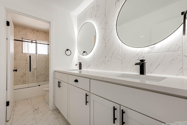 full bath with marble finish floor, shower / bath combination with glass door, double vanity, toilet, and a sink