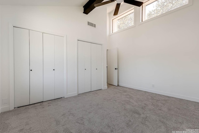 unfurnished bedroom with high vaulted ceiling, carpet floors, visible vents, beamed ceiling, and two closets