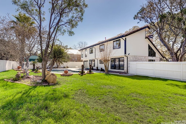 rear view of house with stone siding, a yard, a fenced backyard, and a fenced in pool