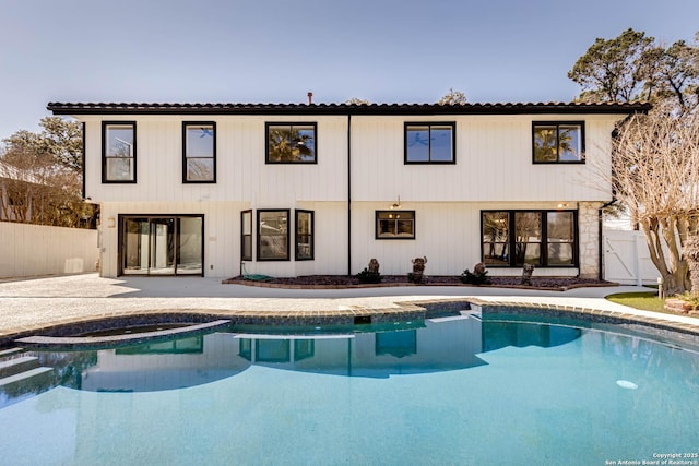 rear view of property featuring an outdoor pool, a patio area, fence, and a gate