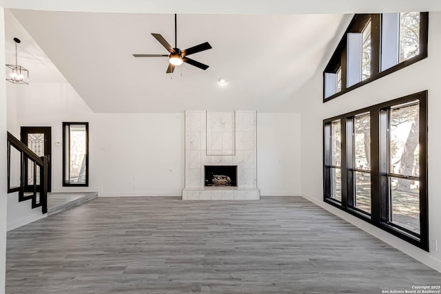 unfurnished living room with high vaulted ceiling, a tile fireplace, wood finished floors, baseboards, and stairway