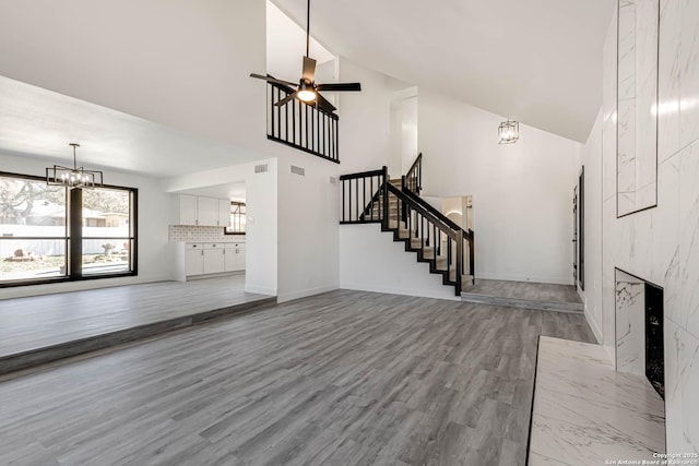 unfurnished living room with high vaulted ceiling, a high end fireplace, stairway, and wood finished floors