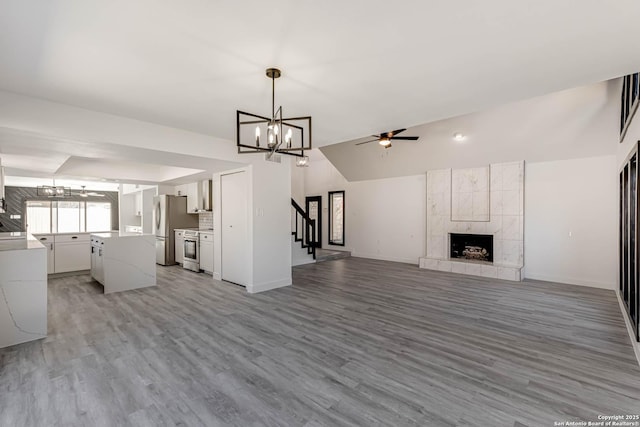 unfurnished living room with vaulted ceiling, light wood finished floors, ceiling fan with notable chandelier, and a tile fireplace