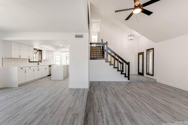 unfurnished living room with light wood-style floors, visible vents, stairway, and baseboards