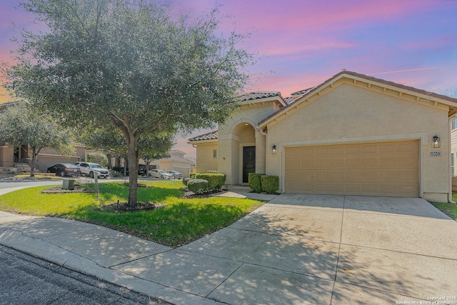 view of front of house with a garage, a tile roof, driveway, stucco siding, and a front lawn