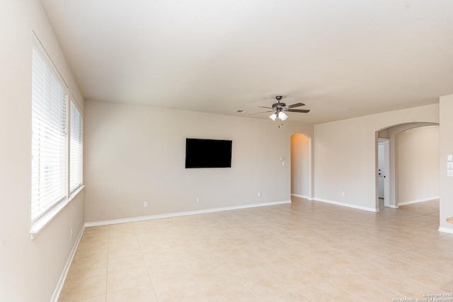 empty room featuring a ceiling fan, arched walkways, and baseboards