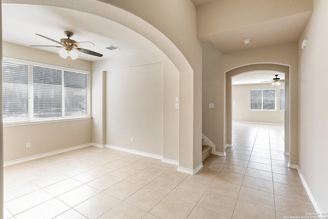 spare room featuring a ceiling fan, arched walkways, baseboards, and light tile patterned floors