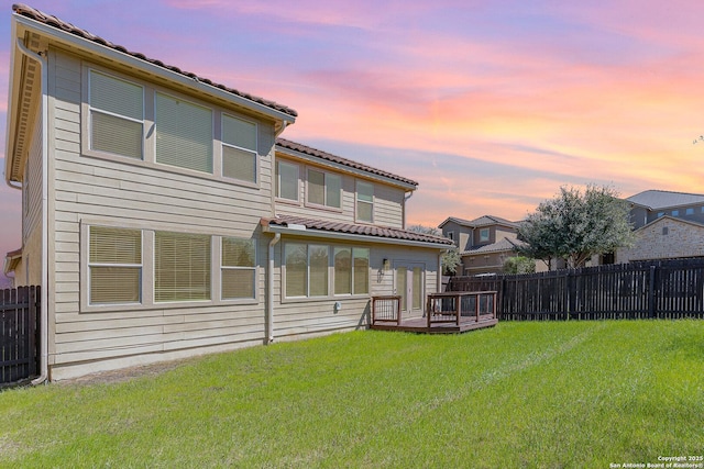 rear view of house featuring a deck, a fenced backyard, a lawn, and a tiled roof