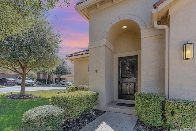 exterior entry at dusk featuring a tile roof and stucco siding