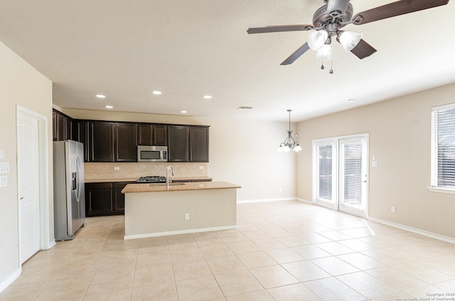 kitchen with light tile patterned floors, a kitchen island with sink, a sink, appliances with stainless steel finishes, and decorative backsplash