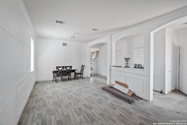 dining room with arched walkways, a decorative wall, wood finished floors, visible vents, and ornamental molding