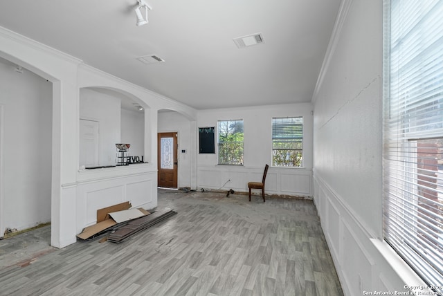 unfurnished room with arched walkways, visible vents, crown molding, and light wood finished floors