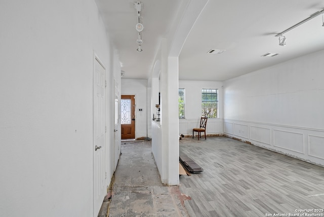 hall featuring arched walkways, visible vents, a decorative wall, wainscoting, and wood finished floors