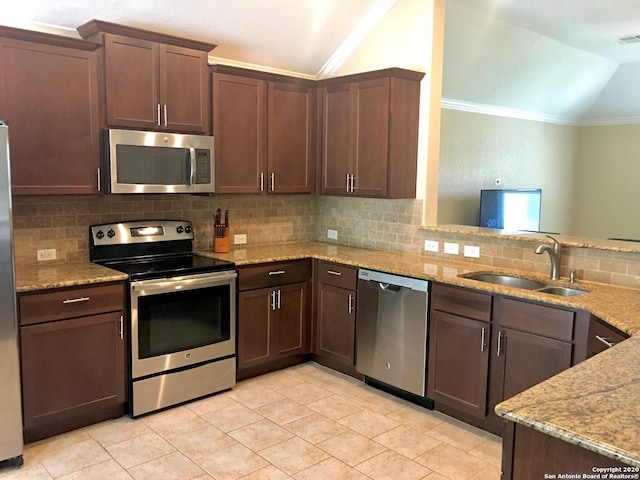 kitchen featuring tasteful backsplash, lofted ceiling, appliances with stainless steel finishes, light stone counters, and a sink