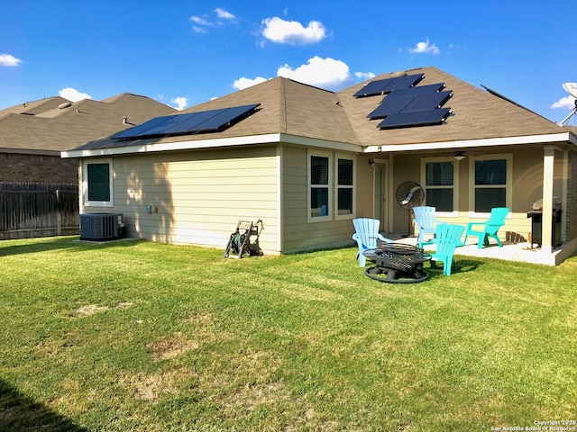 back of house with central air condition unit, a lawn, roof mounted solar panels, fence, and ceiling fan