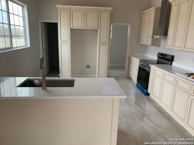 kitchen featuring black electric range, light countertops, wall chimney range hood, and cream cabinetry