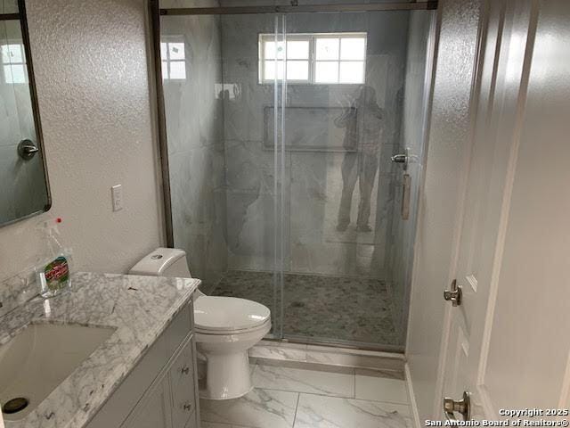 bathroom featuring marble finish floor, a marble finish shower, a textured wall, toilet, and vanity