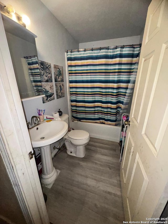 full bath featuring wood finished floors, toilet, and shower / tub combo with curtain