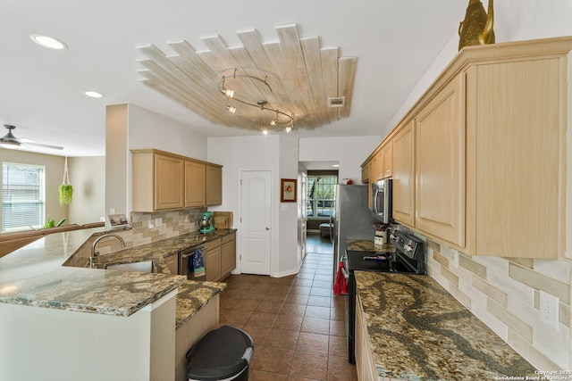 kitchen featuring backsplash, light brown cabinetry, appliances with stainless steel finishes, a sink, and dark stone countertops