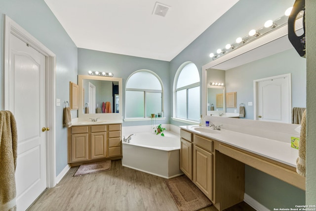 full bathroom featuring a garden tub, two vanities, visible vents, a sink, and wood finished floors