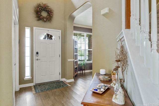 foyer featuring stairway, baseboards, arched walkways, and wood finished floors