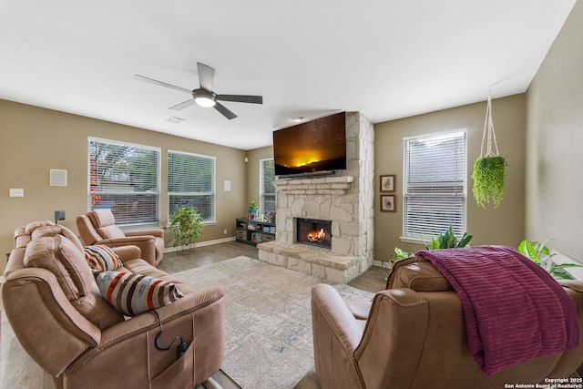 living area featuring ceiling fan, a stone fireplace, wood finished floors, visible vents, and baseboards