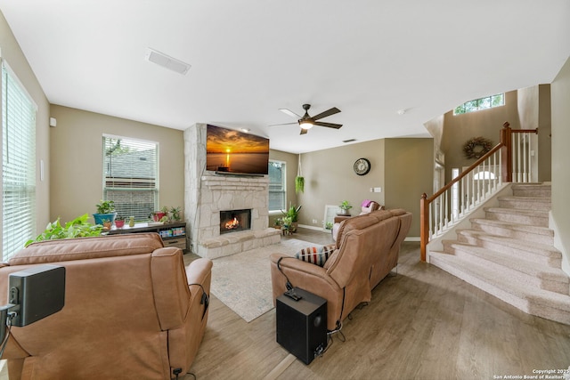 living area featuring a stone fireplace, stairway, light wood-style flooring, and visible vents