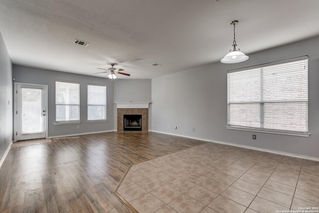 unfurnished living room with a fireplace, visible vents, a ceiling fan, wood finished floors, and baseboards