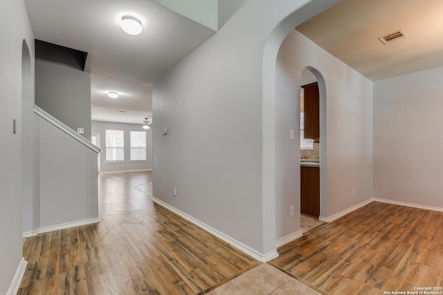 hallway featuring arched walkways, wood finished floors, visible vents, and baseboards