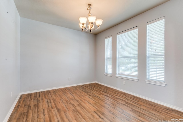 unfurnished room featuring wood finished floors, baseboards, and an inviting chandelier