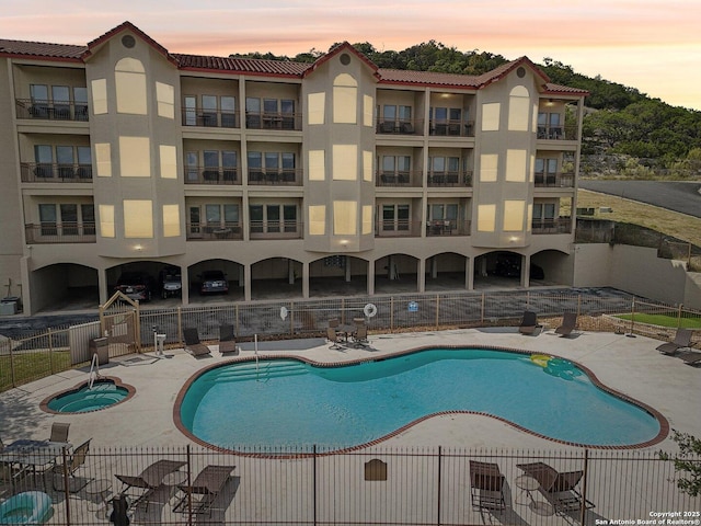 pool at dusk featuring fence, a community pool, and a patio