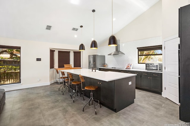 kitchen with light countertops, visible vents, backsplash, appliances with stainless steel finishes, and wall chimney exhaust hood