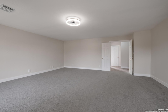 empty room with baseboards, visible vents, and dark colored carpet