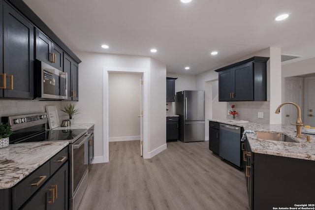 kitchen with a sink, baseboards, light wood-style floors, appliances with stainless steel finishes, and light stone countertops