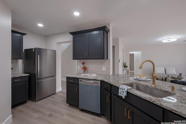 kitchen with appliances with stainless steel finishes, light wood-style floors, a sink, and light stone countertops