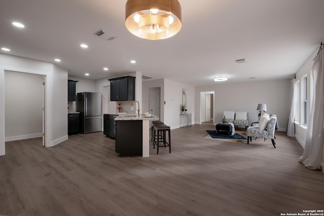 kitchen featuring light wood finished floors, visible vents, open floor plan, freestanding refrigerator, and a kitchen bar