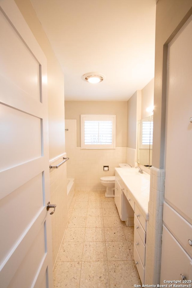 bathroom featuring toilet, a wainscoted wall, a washtub, vanity, and tile walls