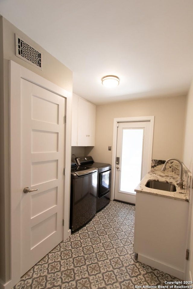 kitchen featuring washing machine and dryer, a sink, visible vents, white cabinets, and light floors