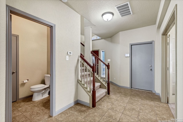 foyer entrance with stairway, visible vents, a textured ceiling, and baseboards