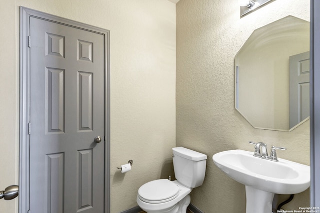 bathroom with toilet, a sink, and a textured wall