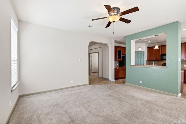 unfurnished room with arched walkways, light carpet, visible vents, baseboards, and a ceiling fan