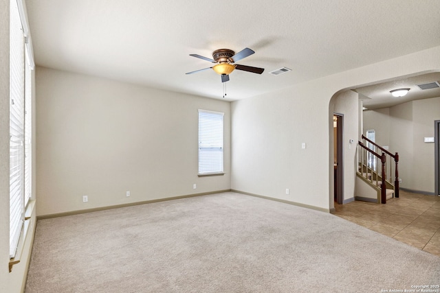 carpeted empty room with arched walkways, visible vents, ceiling fan, and stairway