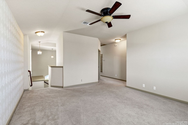 carpeted empty room with wallpapered walls, baseboards, visible vents, and a ceiling fan