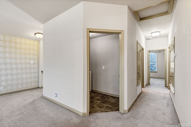 hall with attic access, light carpet, a textured ceiling, baseboards, and wallpapered walls