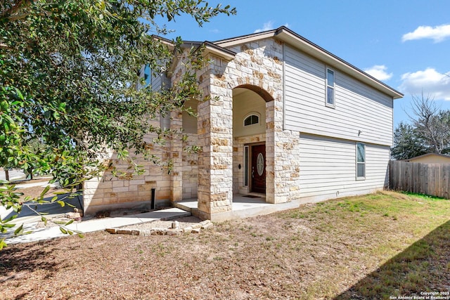 view of front of property featuring a front yard, stone siding, and fence