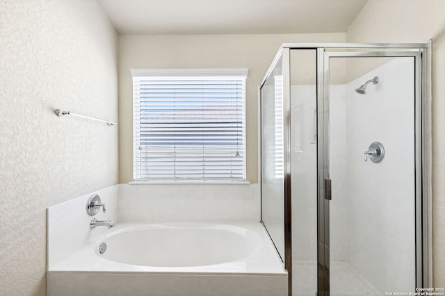 bathroom featuring a textured wall, a stall shower, and a bath